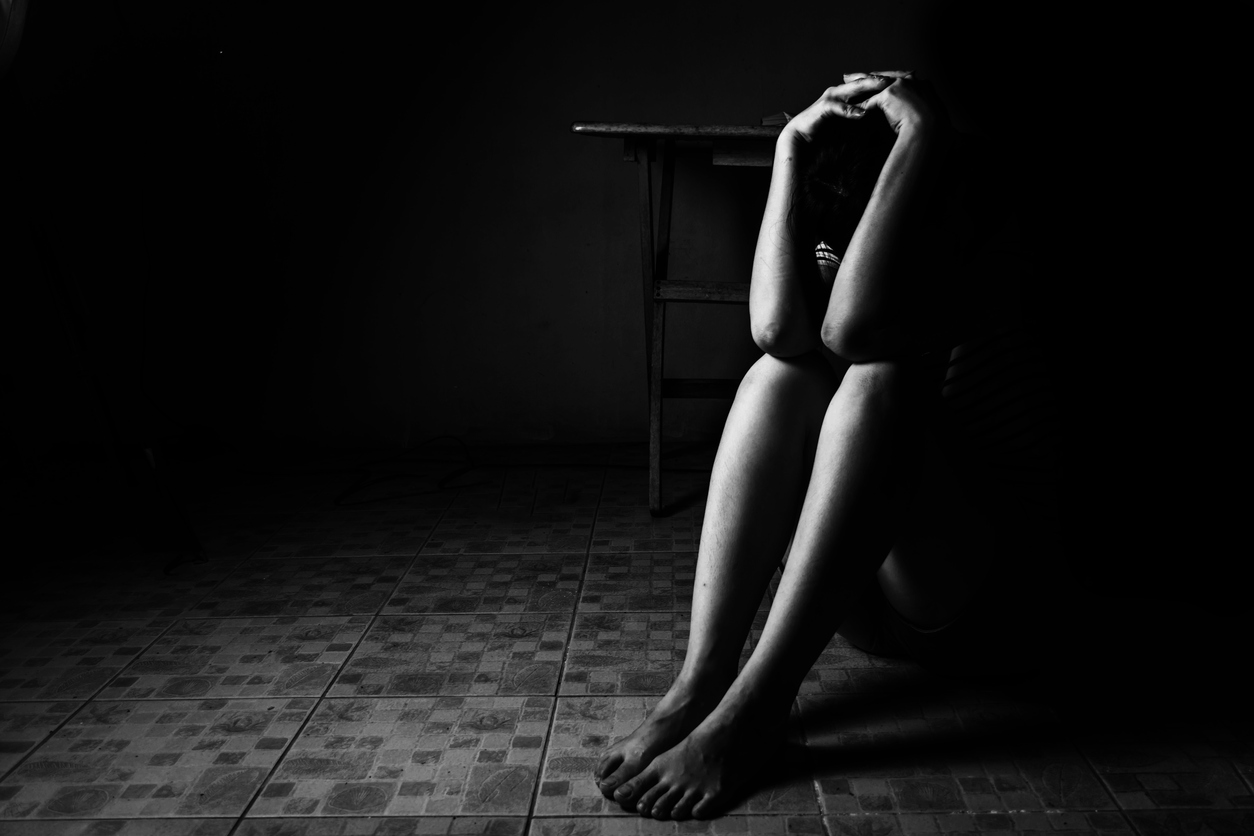 a woman sitting on ground with arm around lower head sexual violence sexual abuse human trafficking concept - ASK LLP - ASK LLP